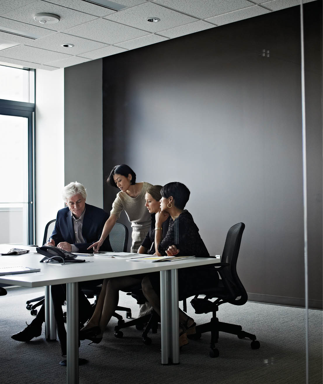 Group of coworkers in discussion in glass walled office conference room businesswoman working on digital table